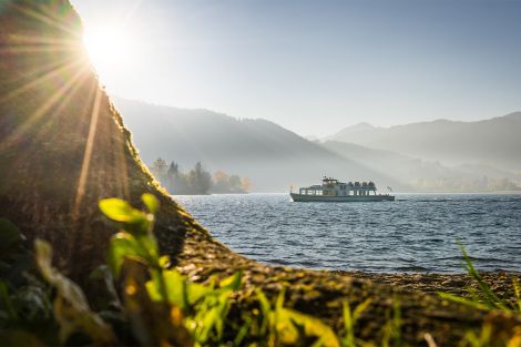 Nahaufnahme eines Golfballs, dahinter ein Schläger auf grünem Gras, im Hintergrund ein Sonnenaufgang